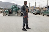 An Afghan policeman with a gun and police truck in the background.