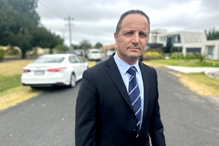 Danny Travaglini, dressed in a suit as he stands in a suburban street.