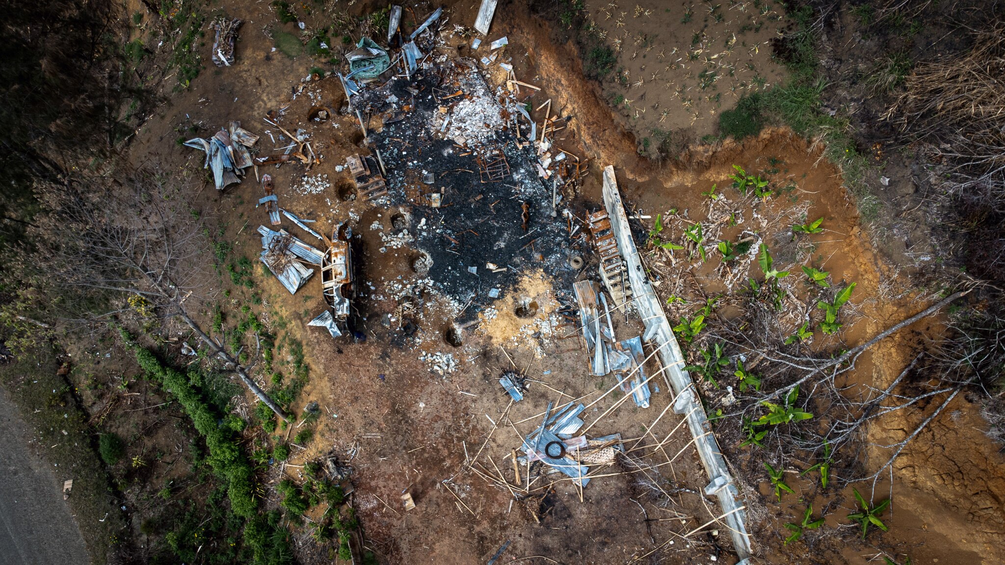 An aerial view shows the charred remains of a building, with sparse trees nearby