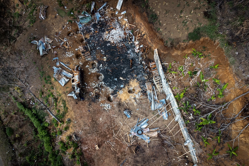 An aerial view shows the charred remains of a building, with sparse trees nearby