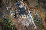 An aerial view shows the charred remains of a building, with sparse trees nearby