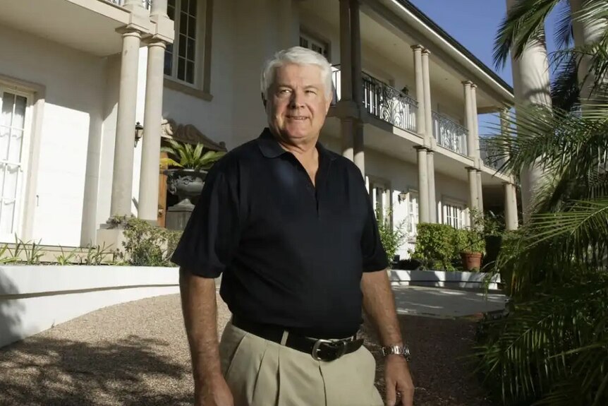 Queensland billionaire property tycoon John Van Lieshout stands outside a mansion.