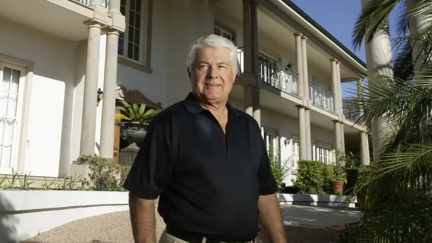 Queensland billionaire property tycoon John Van Lieshout stands outside a mansion.