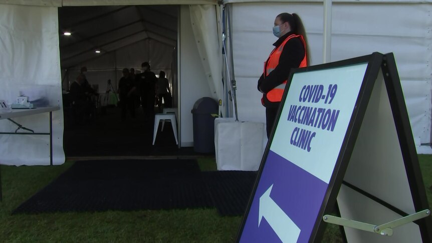 A covid vaccination sign pointing into a marquee tent with a worker standing nearby