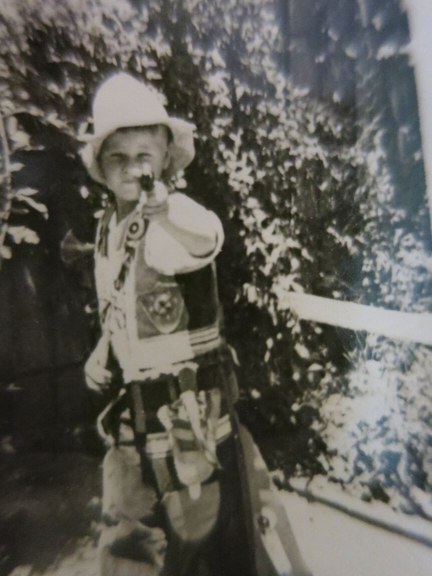 Black and white photo of a boy in a cowboy outfit holding a toy gun