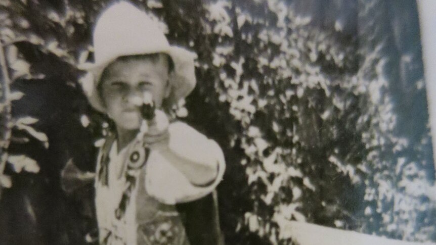 Black and white photo of a boy in a cowboy outfit holding a toy gun