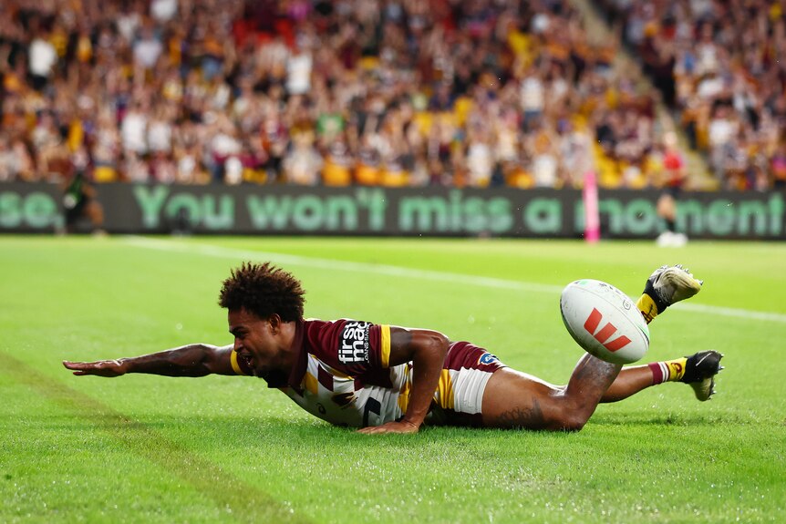 A Brisbane Broncos player lies in the in-goal, acting as if he is swimming after a try.