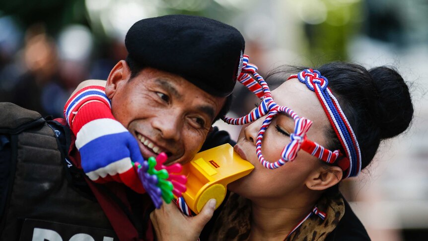 An anti-government protester blows on a whistle next to a riot policeman in Bangkok.