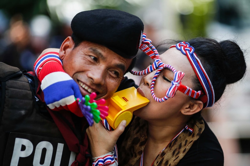 An anti-government protester blows on a whistle next to a riot policeman in Bangkok.