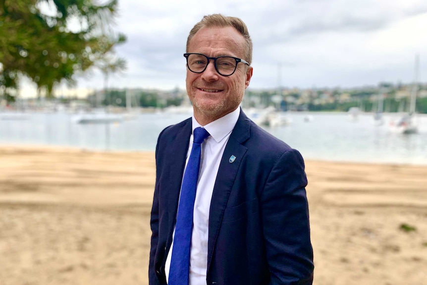Sydney FC chief executive Danny Townsend stands, wearing a suit, at the beach side.