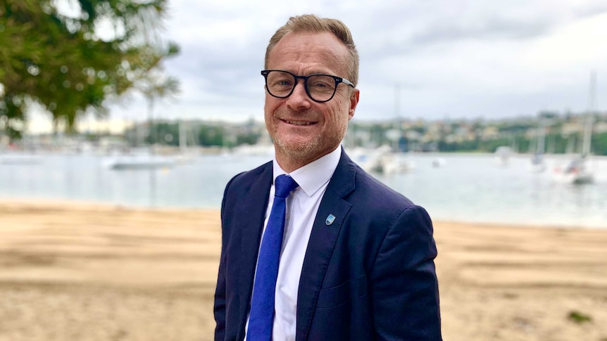 A-League chief executive Danny Townsend stands, wearing a suit, at the beach side.