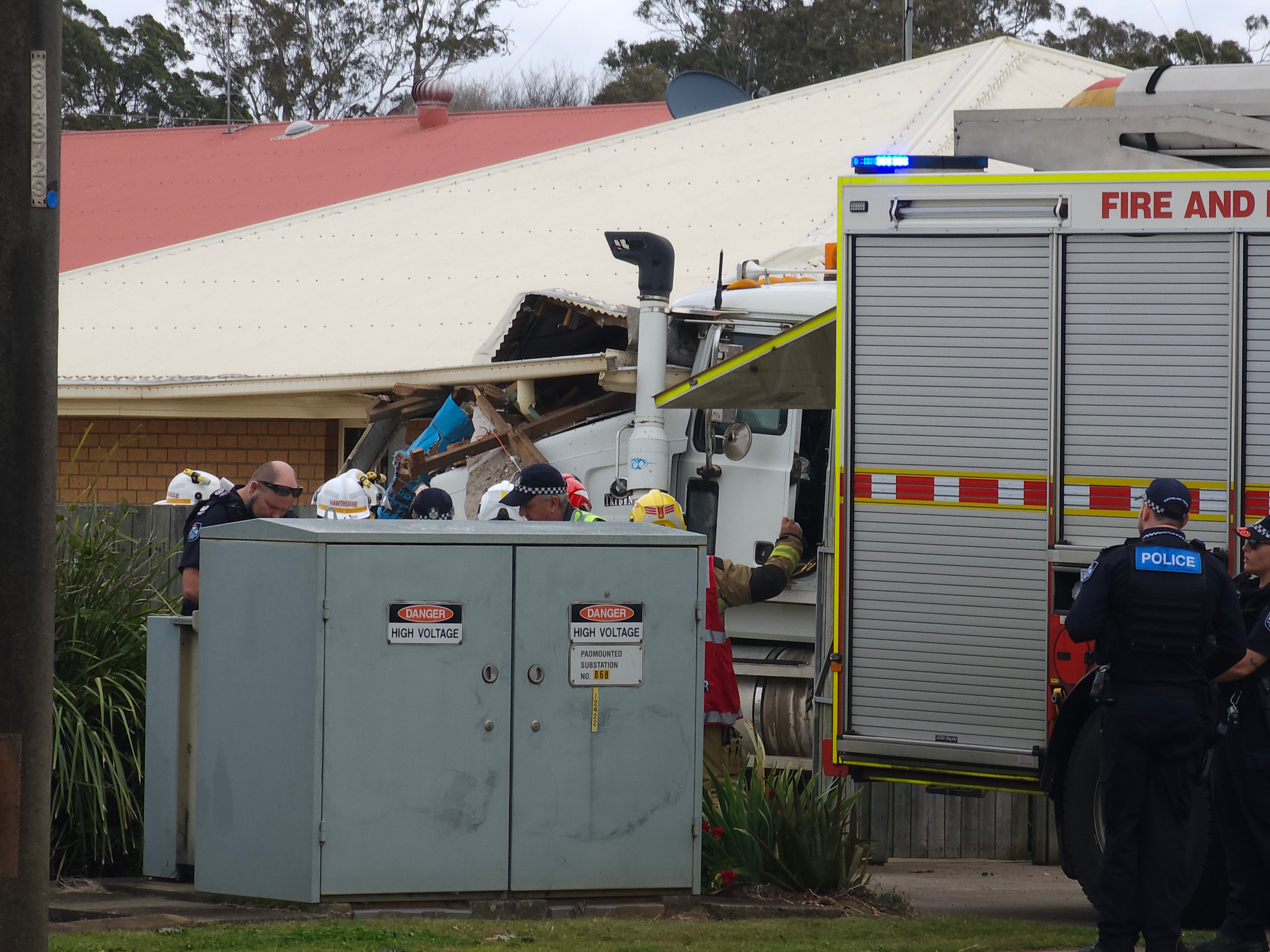 crashed truck into a house with a fire truck and police officer in the foreground 