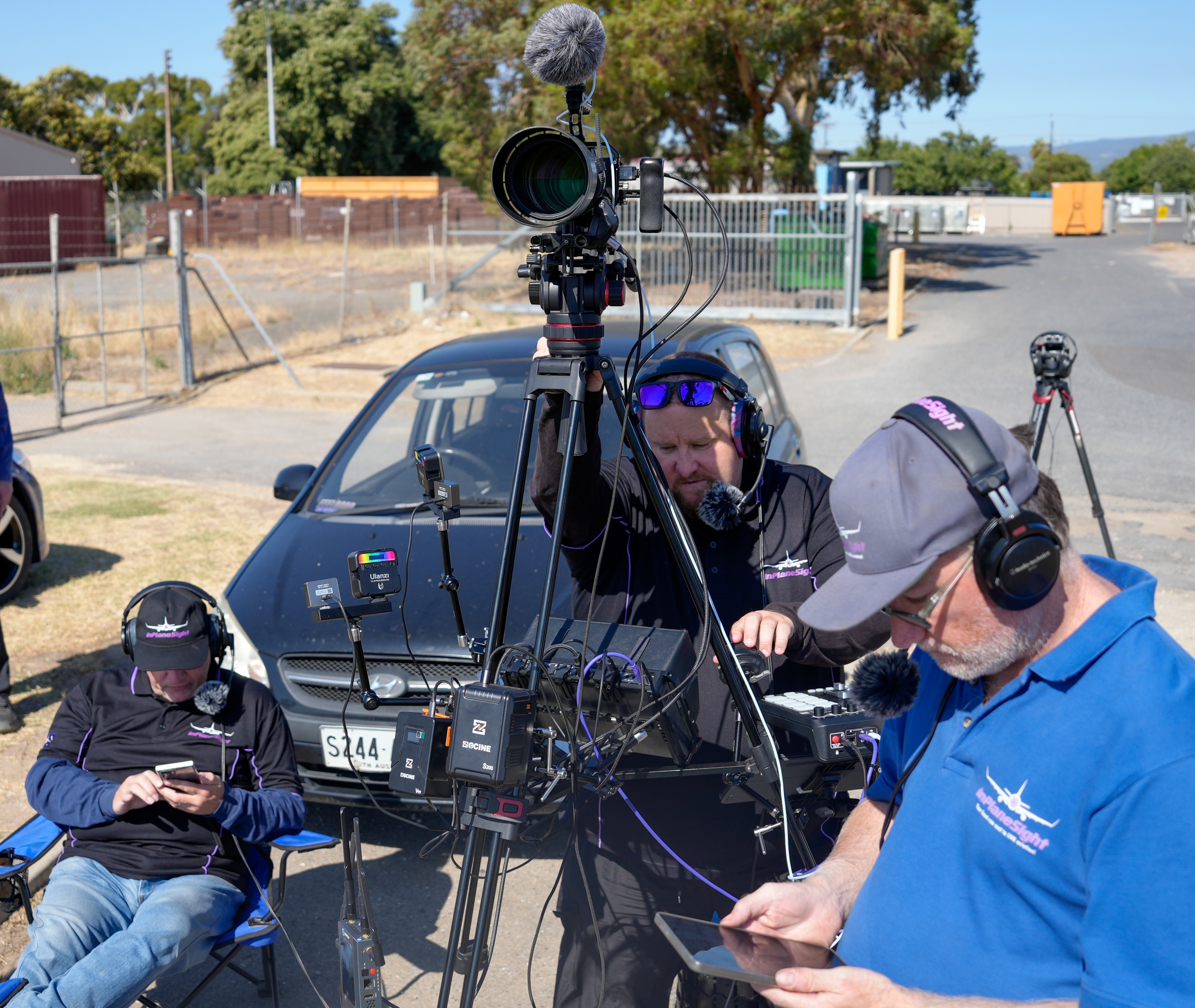 Personas con equipo de cámara frente a un auto negro