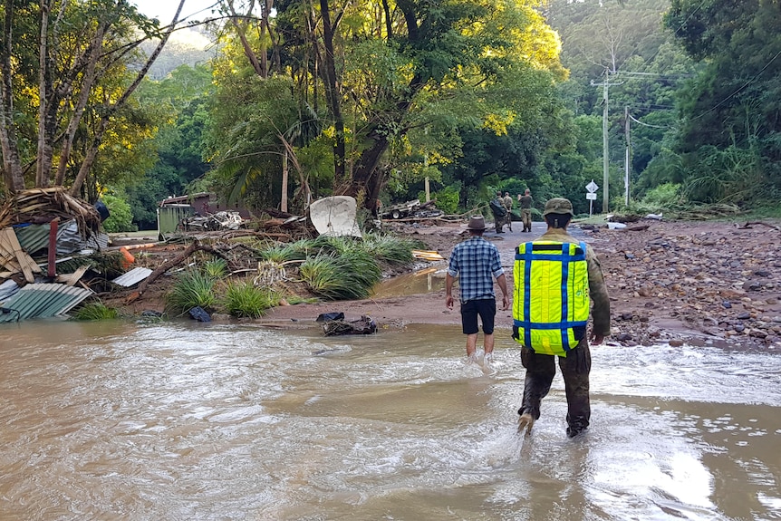 Man in army uniform standing in floodwaters with locals in front of him.