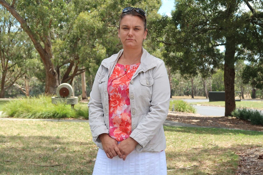 Katrina Beer stands outside wearing a floral top and beige jacket.