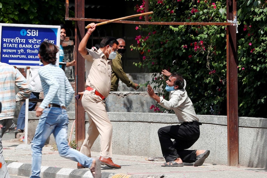 A police officer raises a baton at a man who, according to police, had broken the social distancing rule.