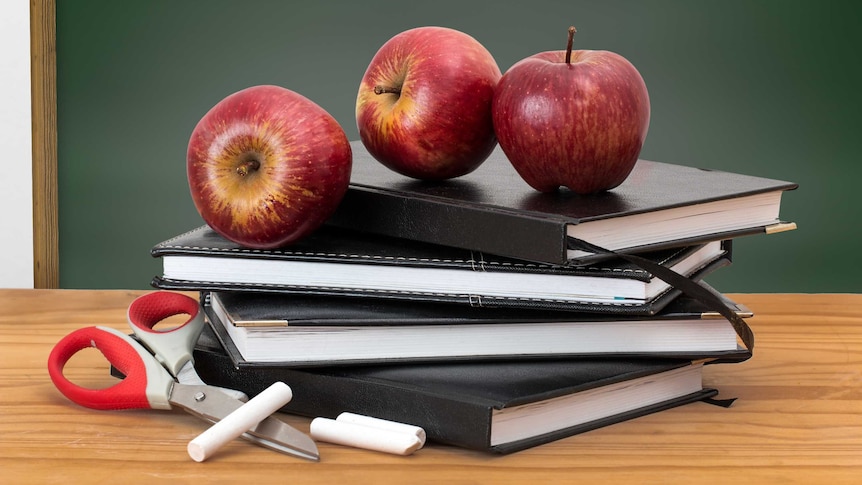 Apples and scissors on some notebooks on a desk.
