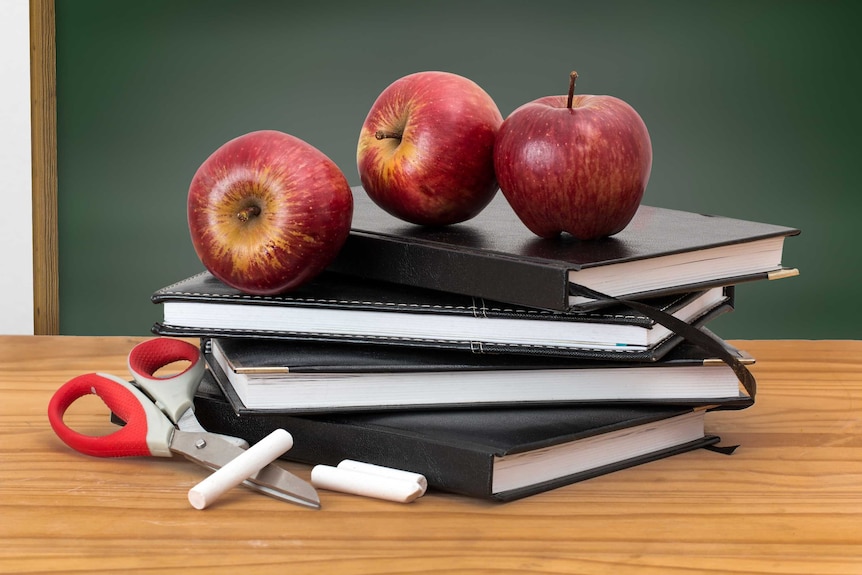 Apples, scissors and chalk on some notebooks on a desk.