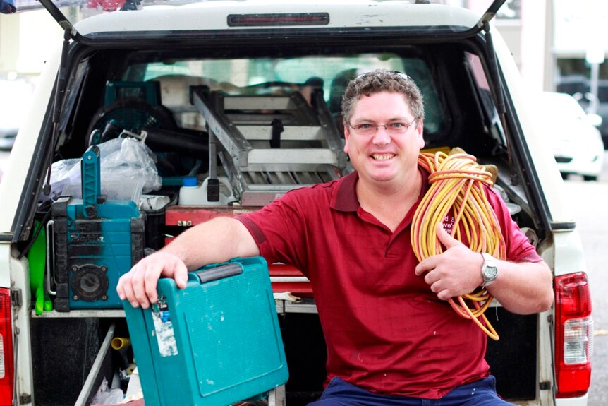 Handyman Dave Crighton sits at the read of his work vehicle holding equipment