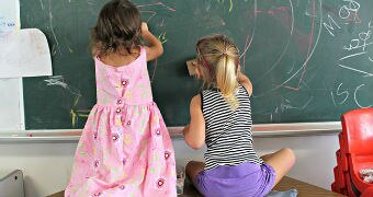 Young girls scribble on chalkboard