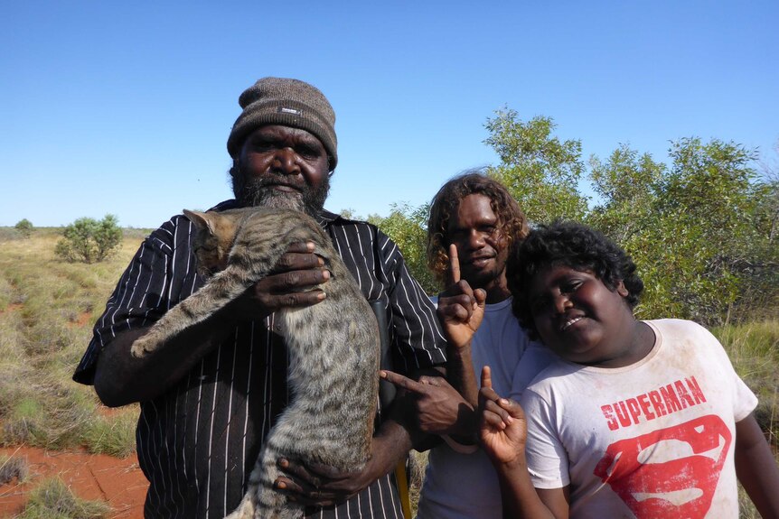 Three people holding up a cat that they caught