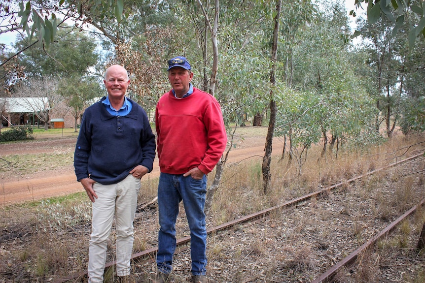 Two men stand in front of a house on an abandoned rail line