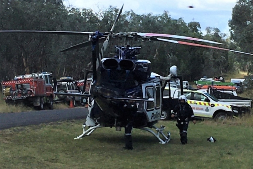 A helicopter, fire truck and many other emergency service vehicles parked beside a rural road