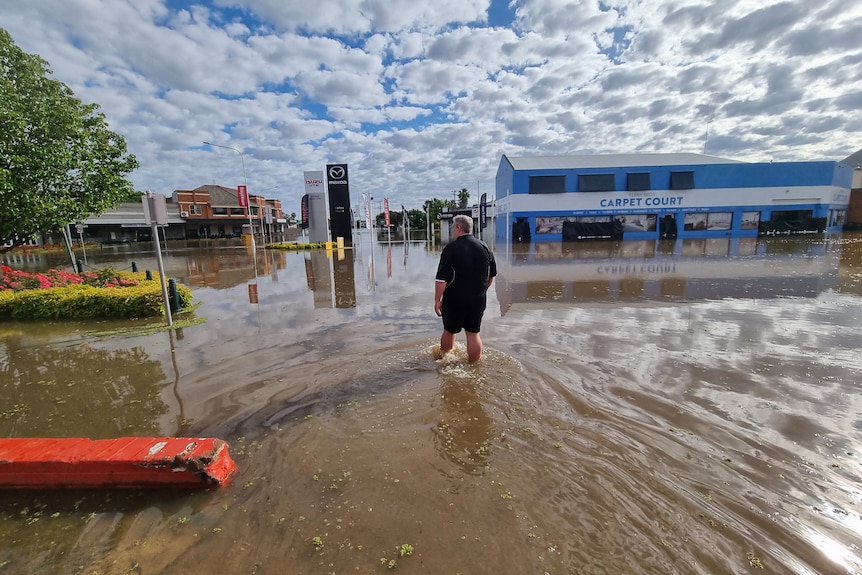 A man walks through floodwaters in the main street of a country town.