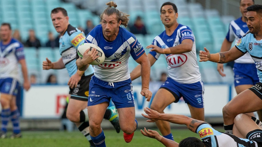 An NRL player evades an opposition tackle and moves downfield ahead of teammates.