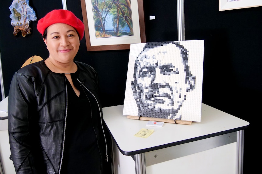 A women in a red hat standing next to a lego portrait of WA premier Mark McGowan. 