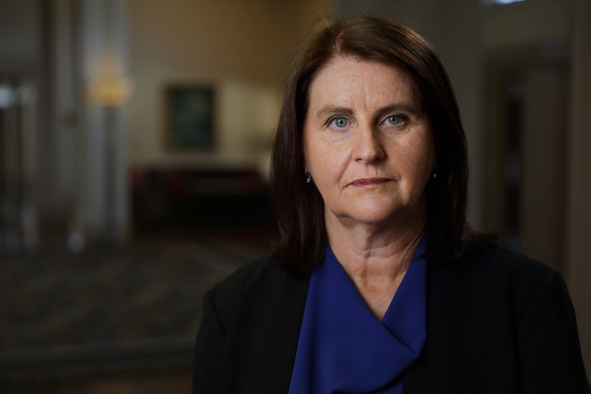 A close portrait of a woman in business attire, who is looking at the camera with a neutral expression.