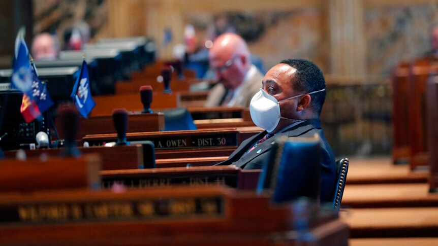一名男子身穿皮衣坐在议会中，面戴口罩。