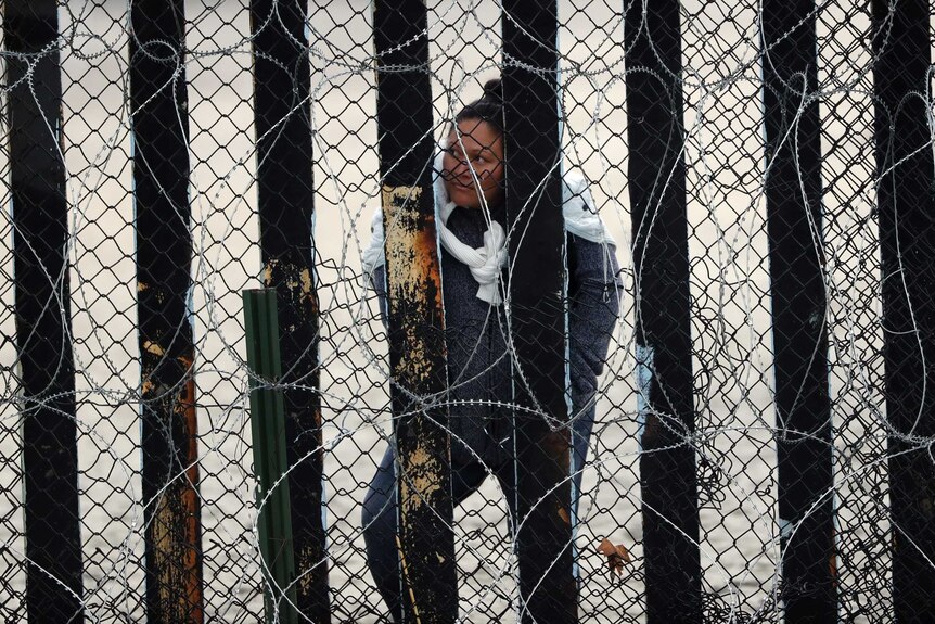 Woman peers through border fence and barbed wires