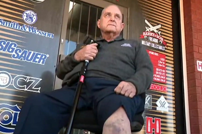 An elderly man holding a crutch shows a large bruise on his knee.