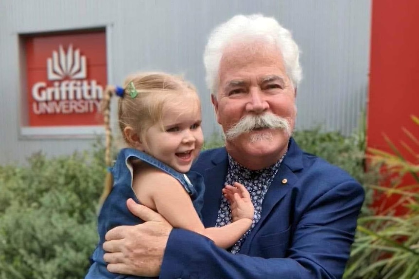 A man with a big moustache with a small girl smiling.