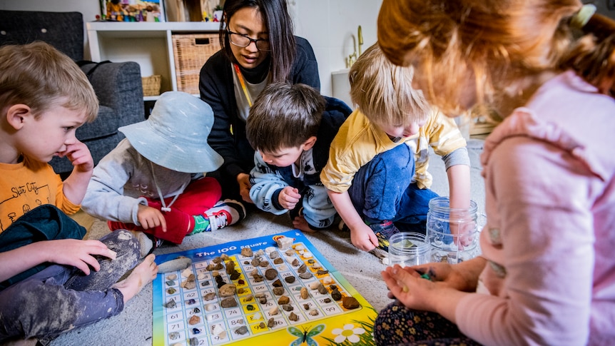 Children and staff are seen around a rug while playing at a child care centre