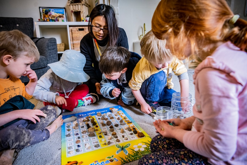 Children and staff are seen around a rug while playing at a child care centre