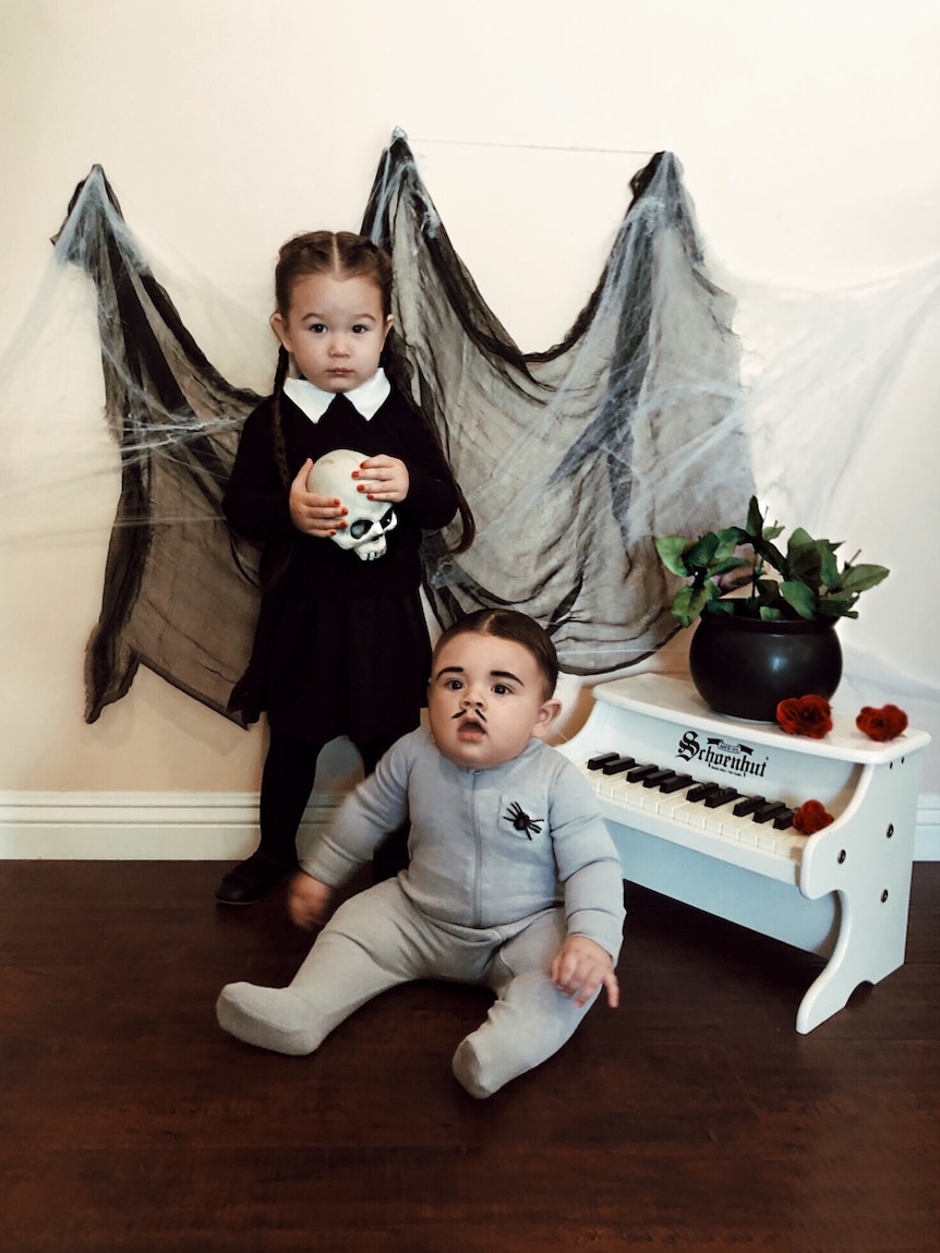 Baby dressed as Pubert and girl dressed as Wednesday from the Addams family movie.