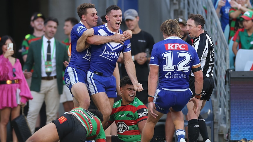 A Bulldogs NRL player yells in celebration as he is hugged from behind by a teammate after a try.