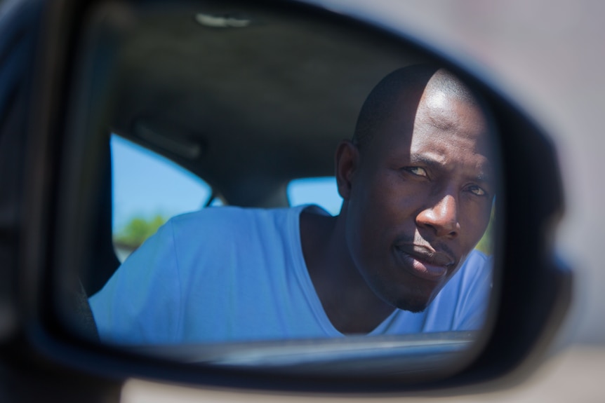 Uber driver Misheck  Mabheka looks in the side mirror of his car.