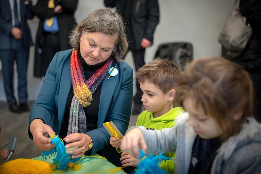 A woman wearing a colourful scarf is pictured making dolls with kids.