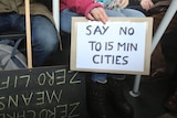 A person on a bus holding a sign that says 'say no to 15 min cities'