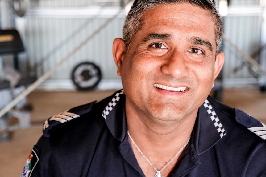 A headshot of a police officer smiling into the camera. He has brown eyes and is greying.