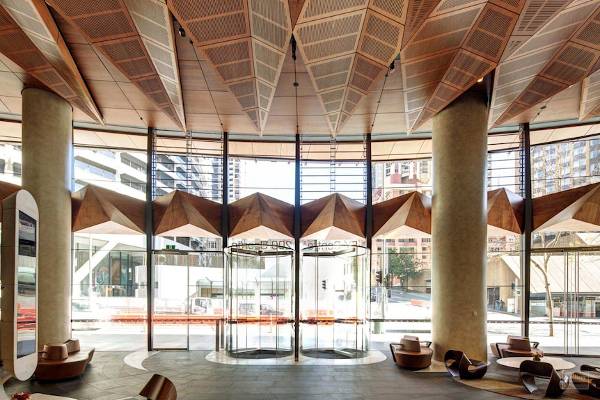 A large lobby with 2 concrete pillars on either side, a wooden roof and tan leather chairs.