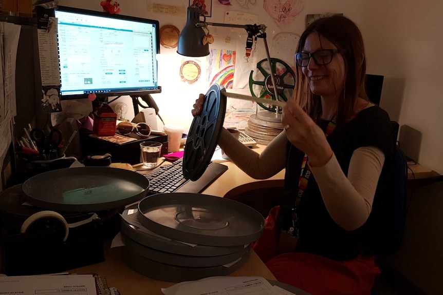 Woman holding reel of film and looking at a section pulled out.