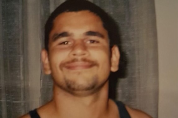 An old colour photo of a young man wearing a black singlet and smiling