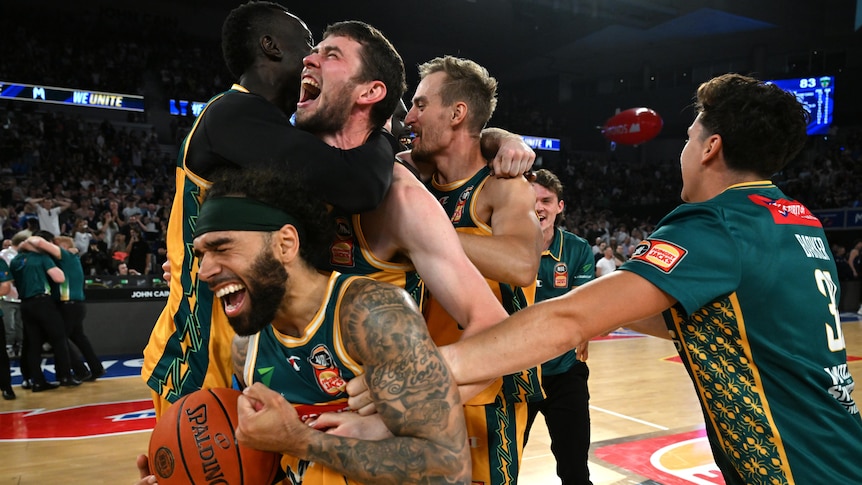 A group of Tasmania NBL players cheer, cry and embrace on the court after winning the title. 