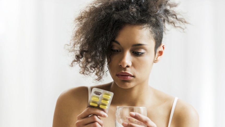 A woman holds a packet of pills and a glass of water.