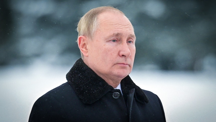 Vladimir Putin looking sombre, dressed in a black coat while standing in the snow 