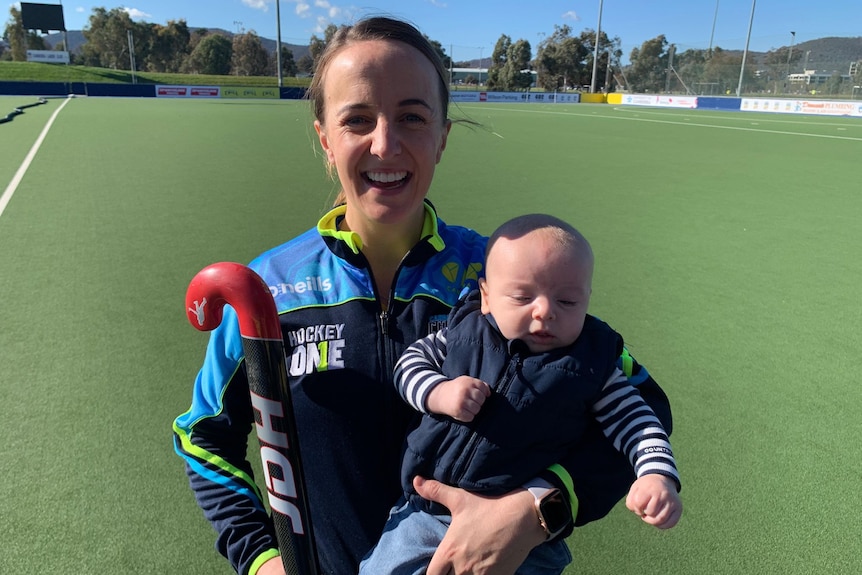 A woman holding a baby and a hockey stick. 